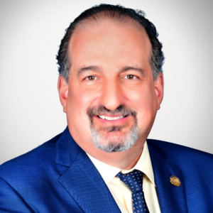 A picture of Bob Goldberg- a man in a blue suit and salt and pepper close cut beard.